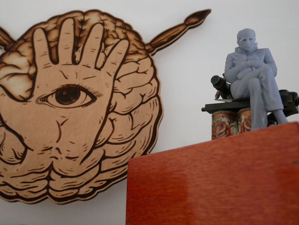 Dettaglio logo forma mentis in legno appeso vicino a miniatura in 3d di uomo seduto su strumento per tatuaggi